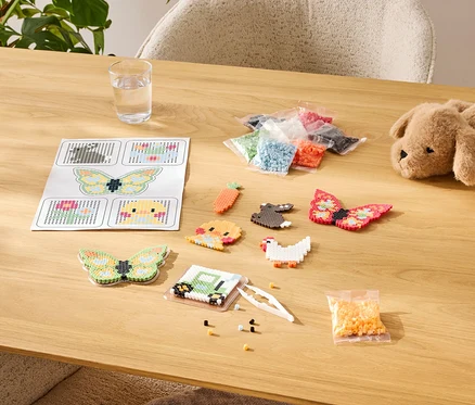 Table avec kit de bricolage de perles à repasser, comprenant des modèles, des motifs finis et des assortiments de couleurs en sachets.