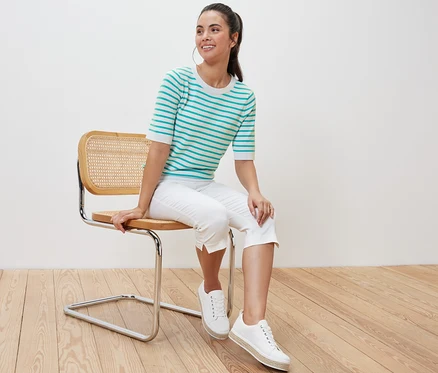 Une femme est assise sur une chaise et porte un pull en maille fine rayé turquoise.