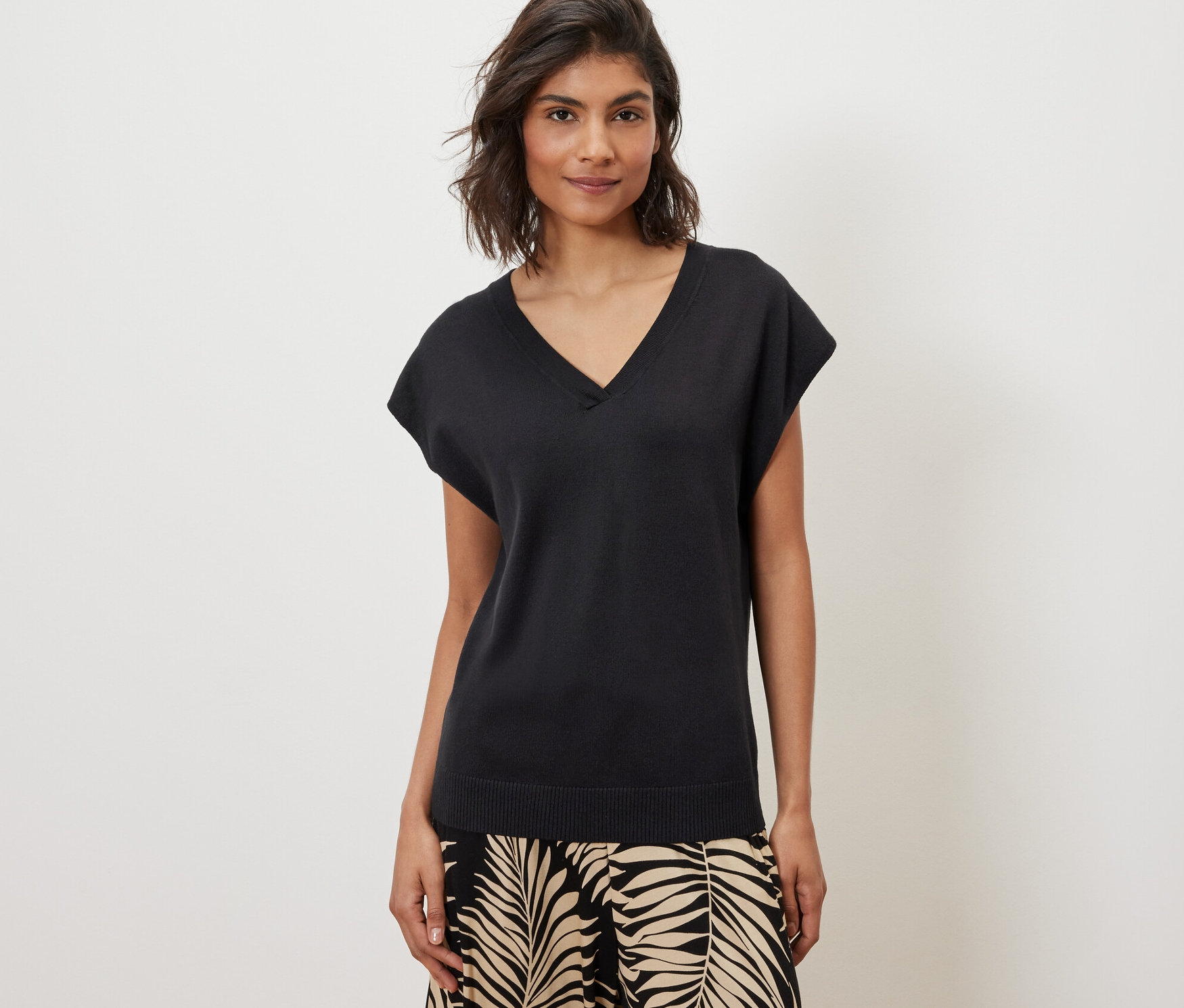 Une femme porte un pull-over en maille fine à manches courtes noir et un pantalon à motifs.