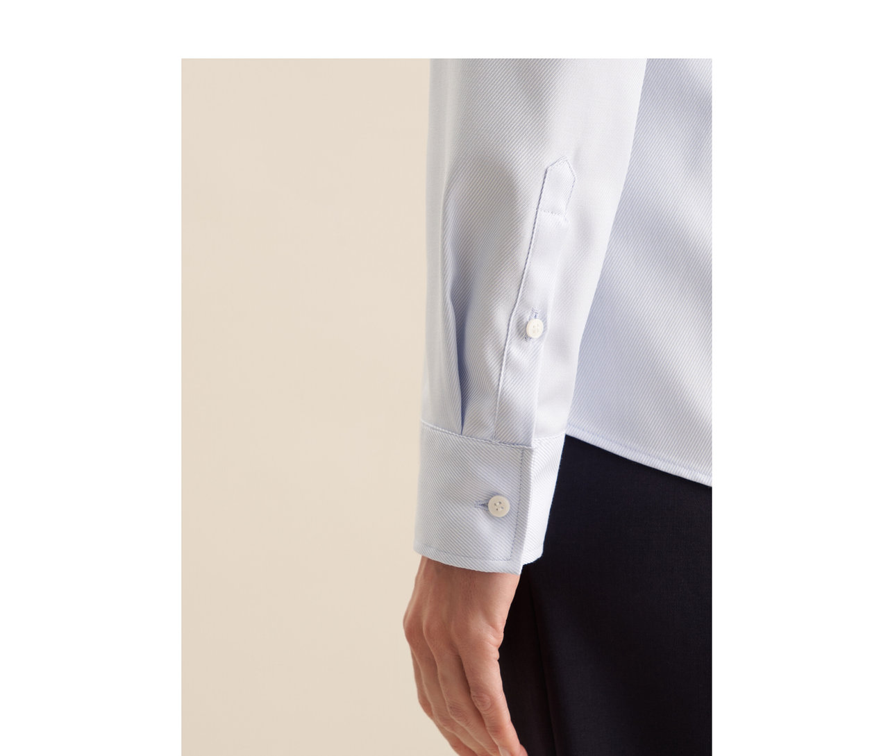 Gros plan sur le bras et la main d'une personne portant un chemisier en twill Seidensticker bleu clair avec un poignet boutonné et un pantalon foncé.