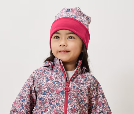 Une fillette souriante porte une veste et un bonnet à fleurs.