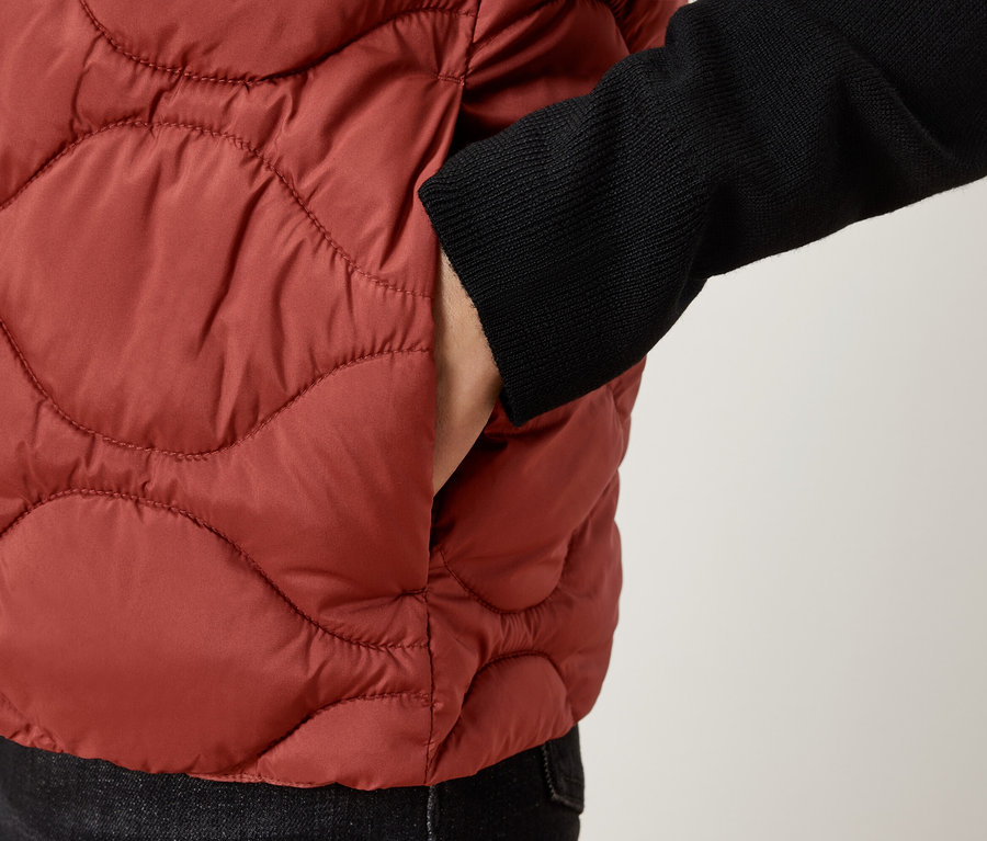 Gros plan d'une personne portant un gilet matelassé marron avec une main dans la poche.