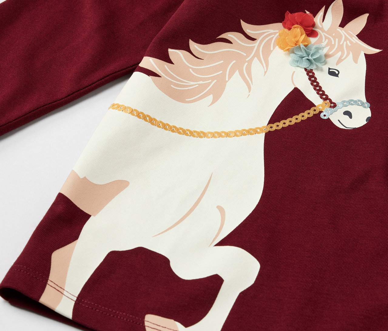 Gros plan sur un t-shirt à manches longues bordeaux pour enfant avec un motif de cheval.