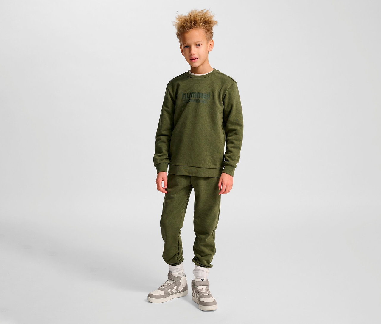 Garçon debout portant un sweat-shirt et un pantalon de survêtement HUMMEL HMLJR Base vert.