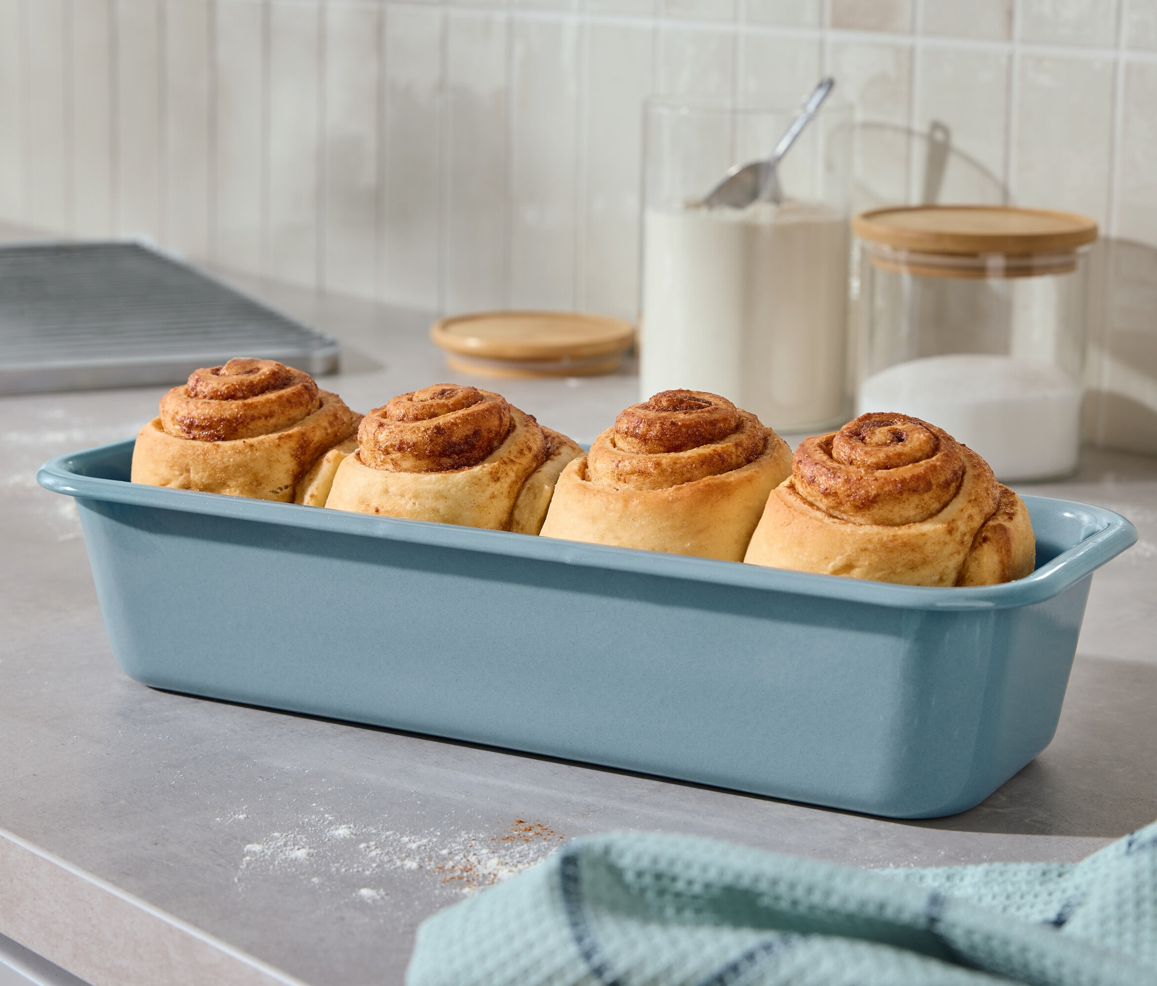 Quatre brioches à la cannelle dans un plat bleu sur un comptoir de cuisine.