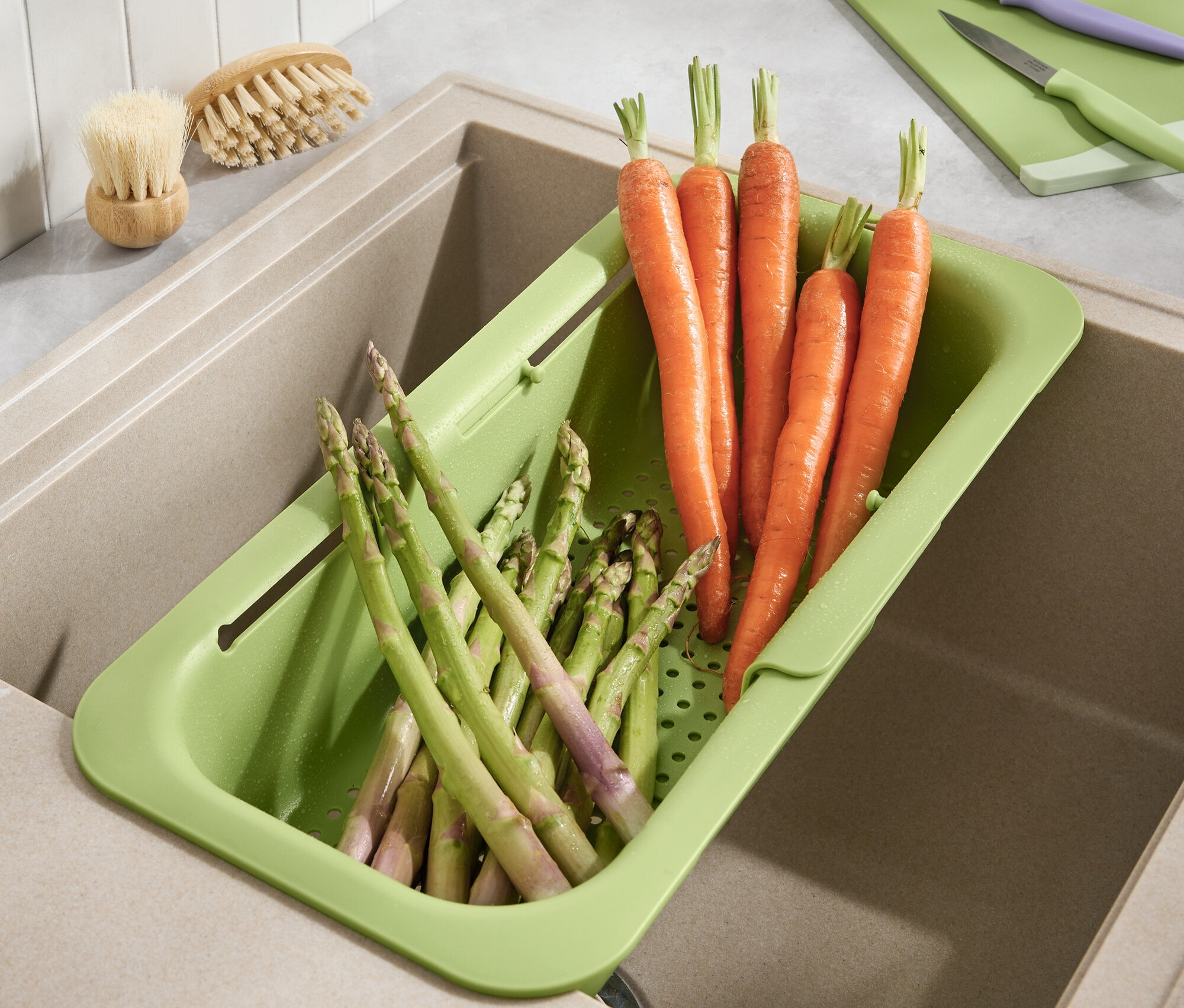 Des carottes et des asperges reposent dans une passoire verte dans l'évier.