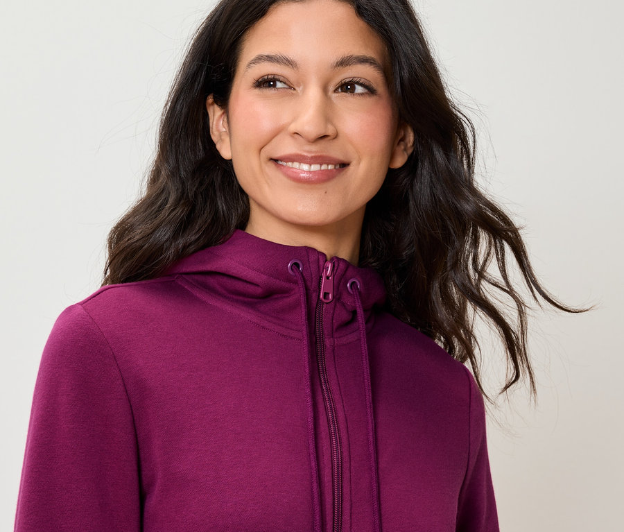 Une femme souriante porte un sweat à capuche violet.