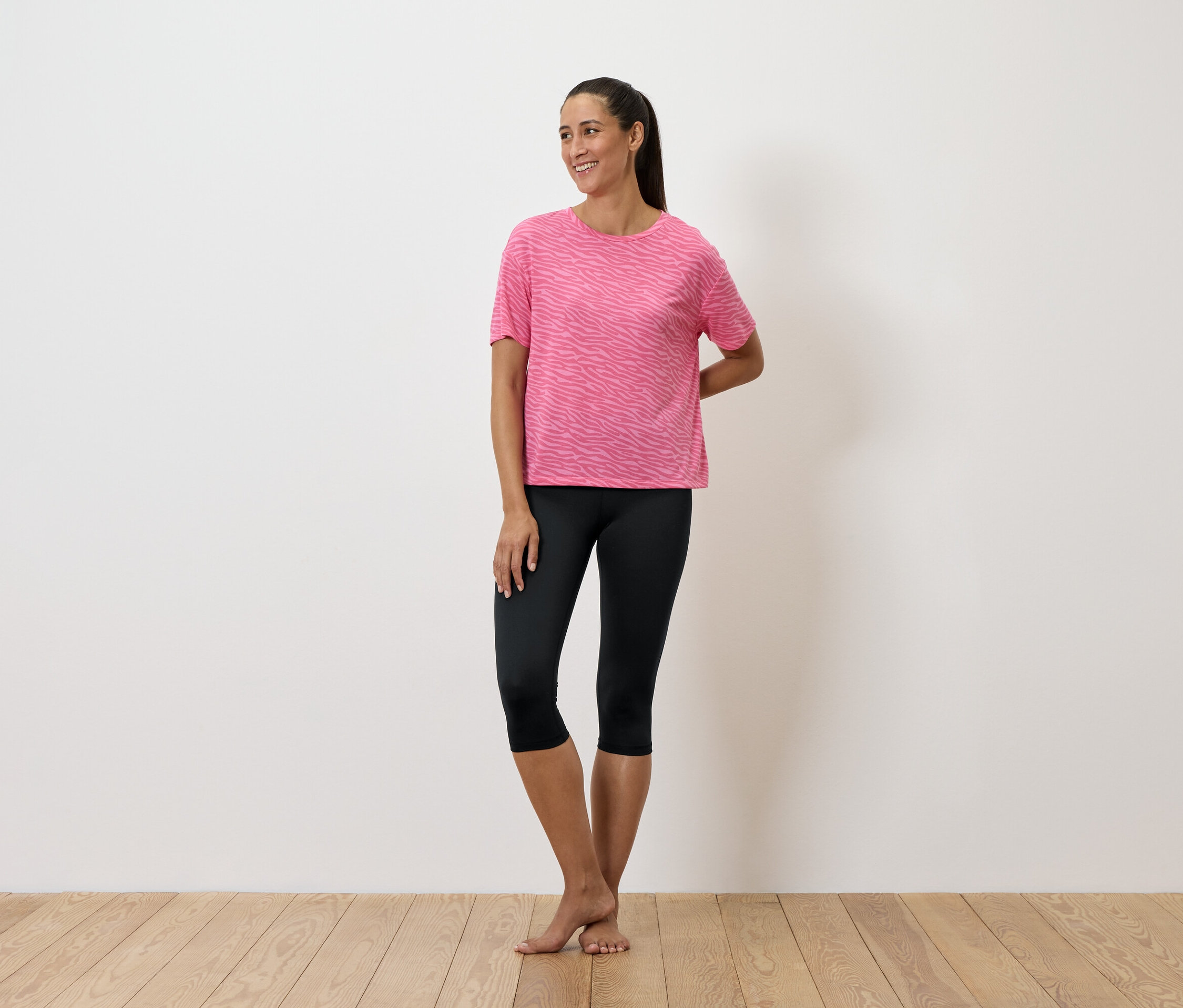 Une femme debout porte un t-shirt rose et un legging noir.