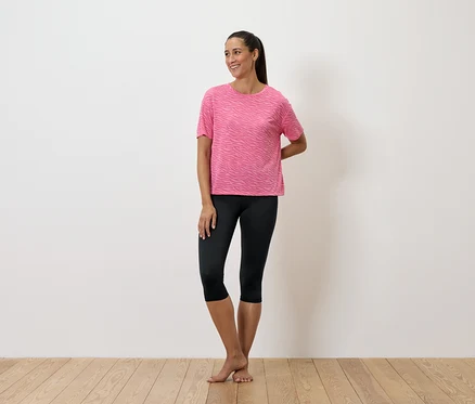 Une femme debout porte un t-shirt rose et un legging noir.