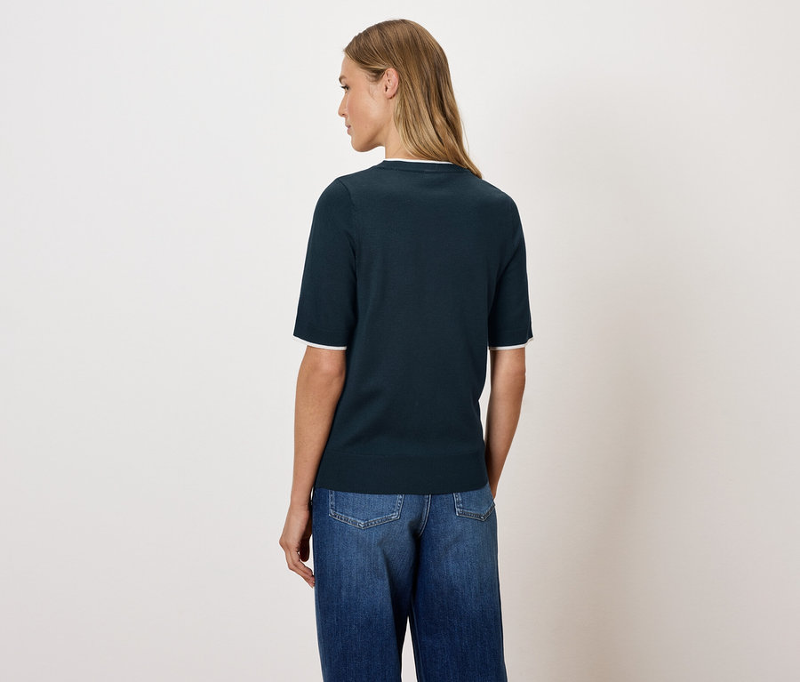 Une femme pose dos à l'appareil photo, portant un haut bleu marine et un jean.