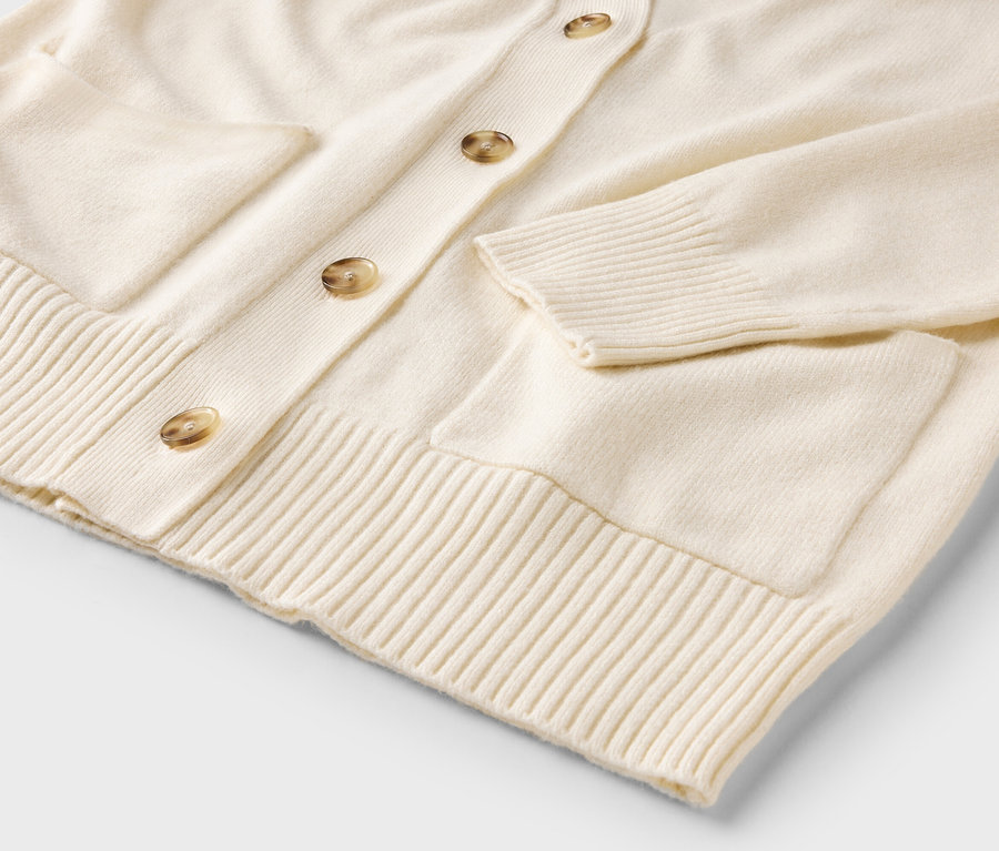 Gros plan sur un cardigan crème boutonné avec poches.