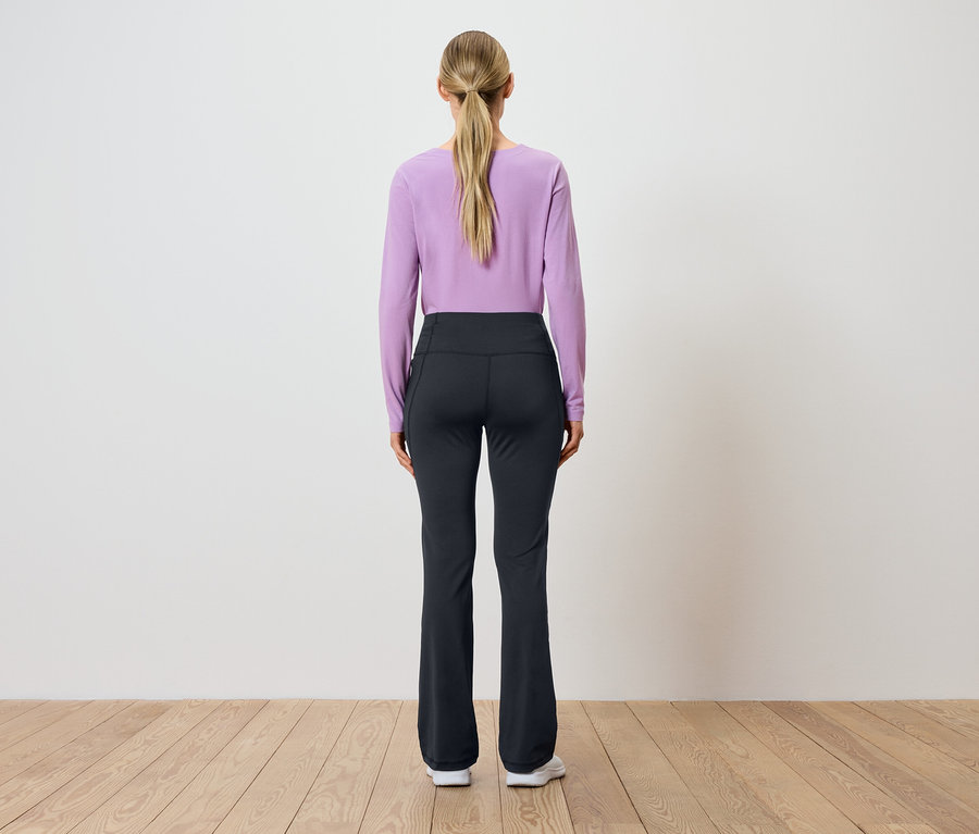 Vue de dos d'une femme aux cheveux blonds attachés en queue de cheval, portant un haut violet à manches longues et un pantalon noir.