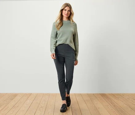 Blonde portant un pull vert et un pantalon gris foncé posant à l'intérieur.