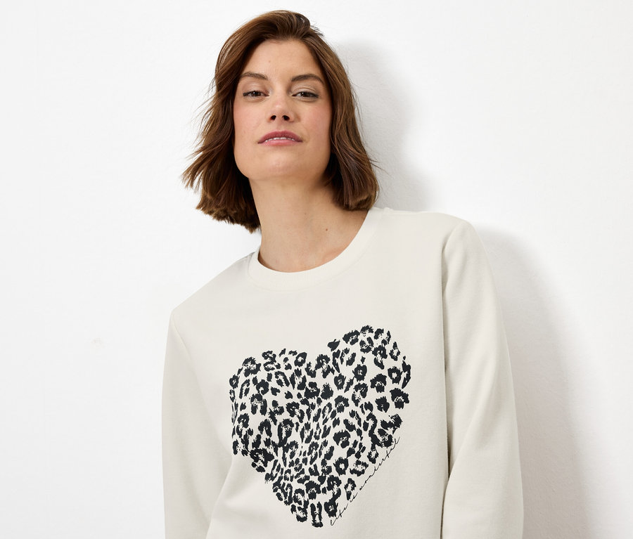 Femme portant un sweat-shirt crème avec un cœur à motif léopard.