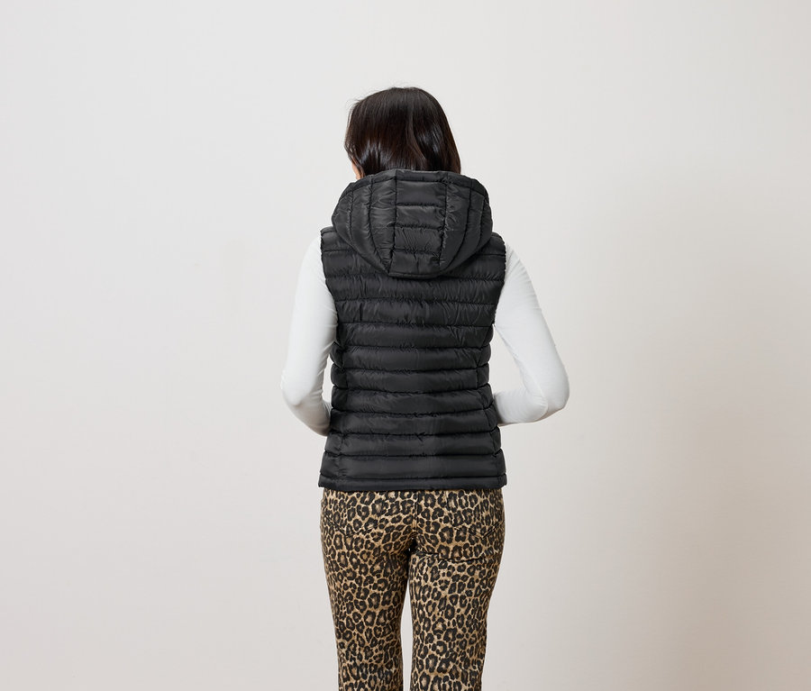 Une femme vue de dos porte un gilet noir matelassé à capuche et un pantalon à motif léopard.