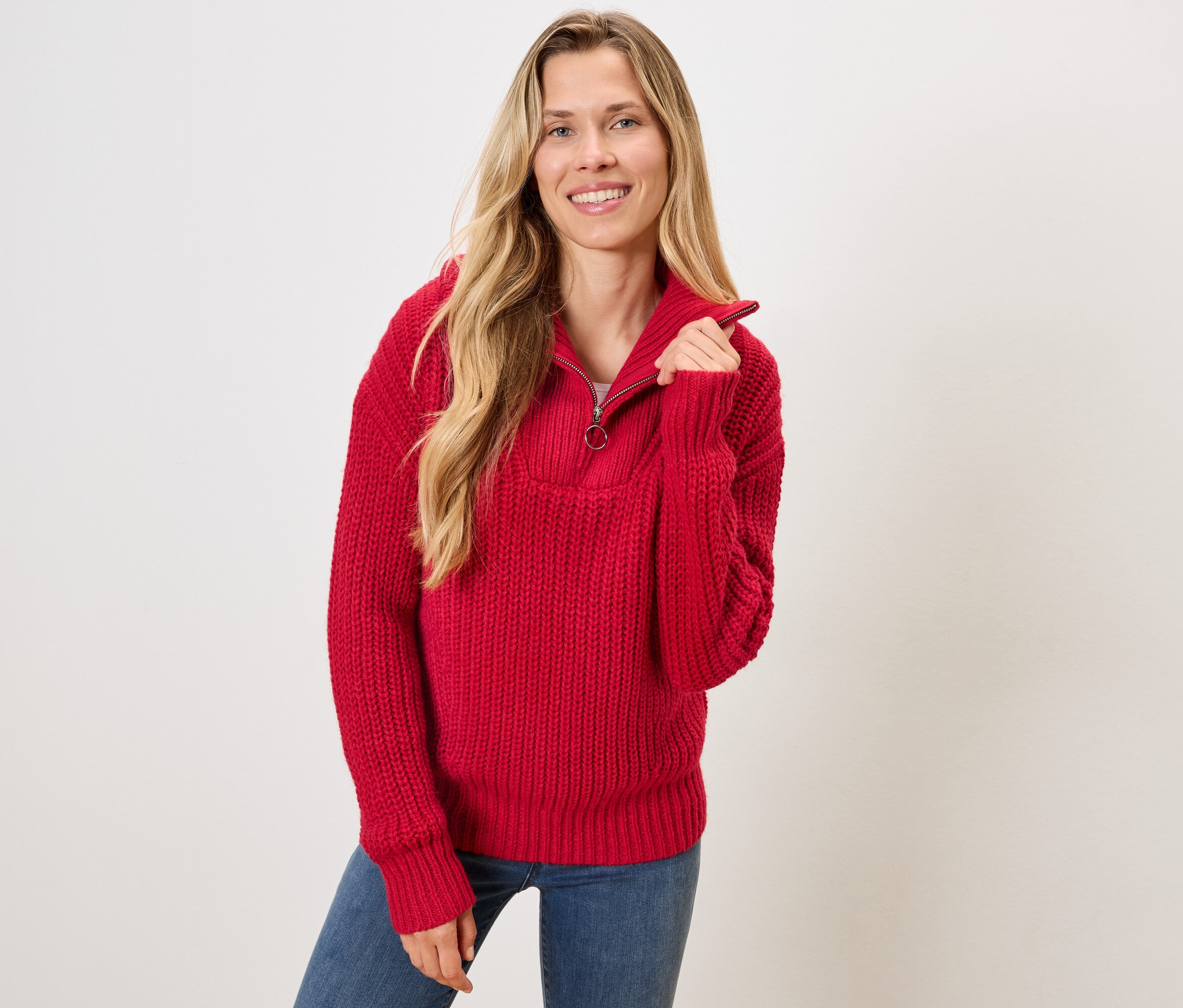 Une femme blonde porte un pull rouge et un jean bleu.