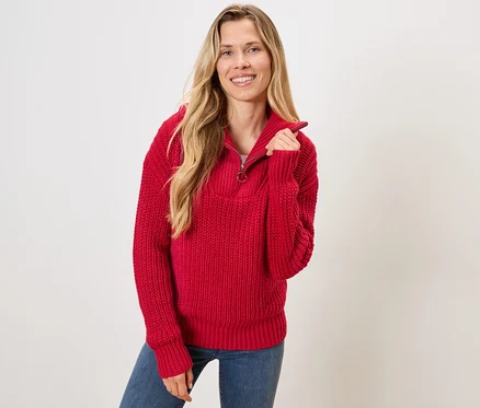 Une femme blonde porte un pull rouge et un jean bleu.