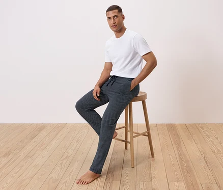 Un homme est assis sur un tabouret, portant un t-shirt blanc et un pantalon à motifs.