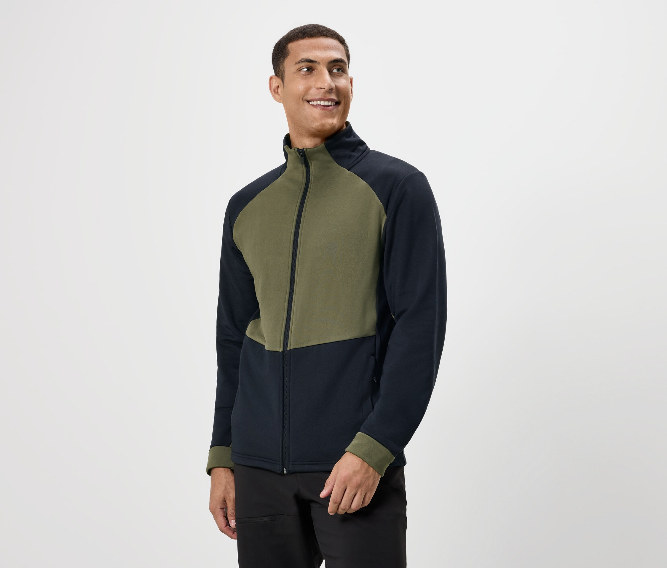 Un homme souriant portant une veste zippée olive et bleu marine.