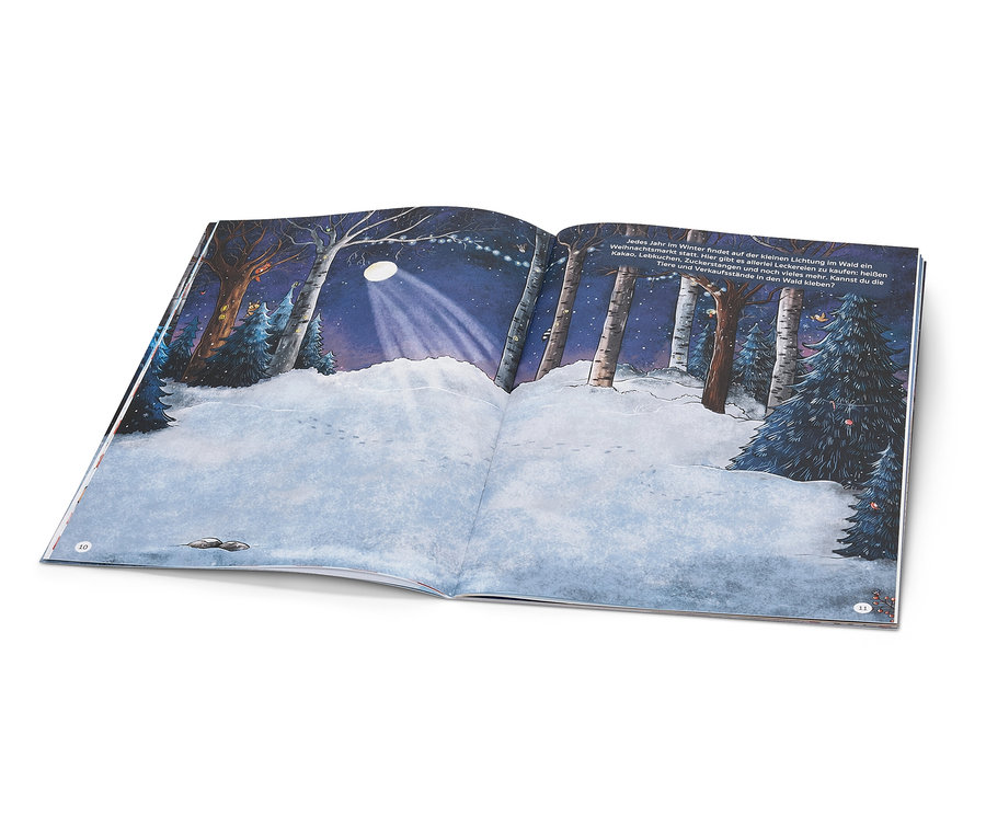 Un livre ouvert montre une scène de forêt enneigée avec une clairière illuminée la nuit.