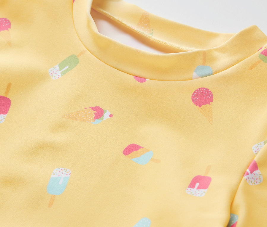 Gros plan sur une combinaison jaune pour enfants avec protection UV 80 et imprimés de glaces.