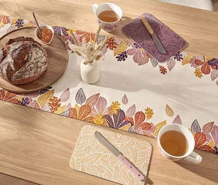 Pain sur une planche en bois et une tasse de thé sur un chemin de table à motif de feuilles.