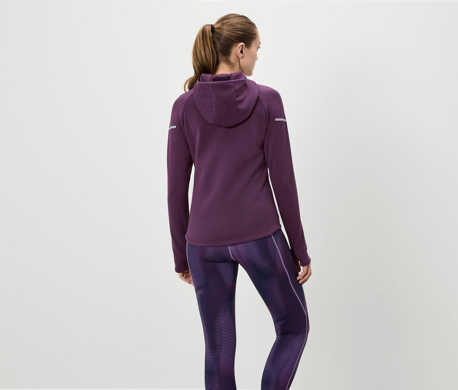 Une femme vue de dos porte un sweat à capuche violet et un legging à motifs.