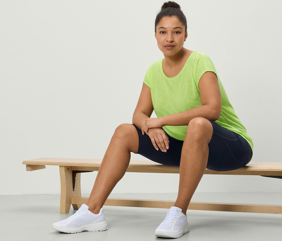 Une femme est assise sur un banc et porte un cycliste de sport bleu foncé et un t-shirt de sport vert citron.