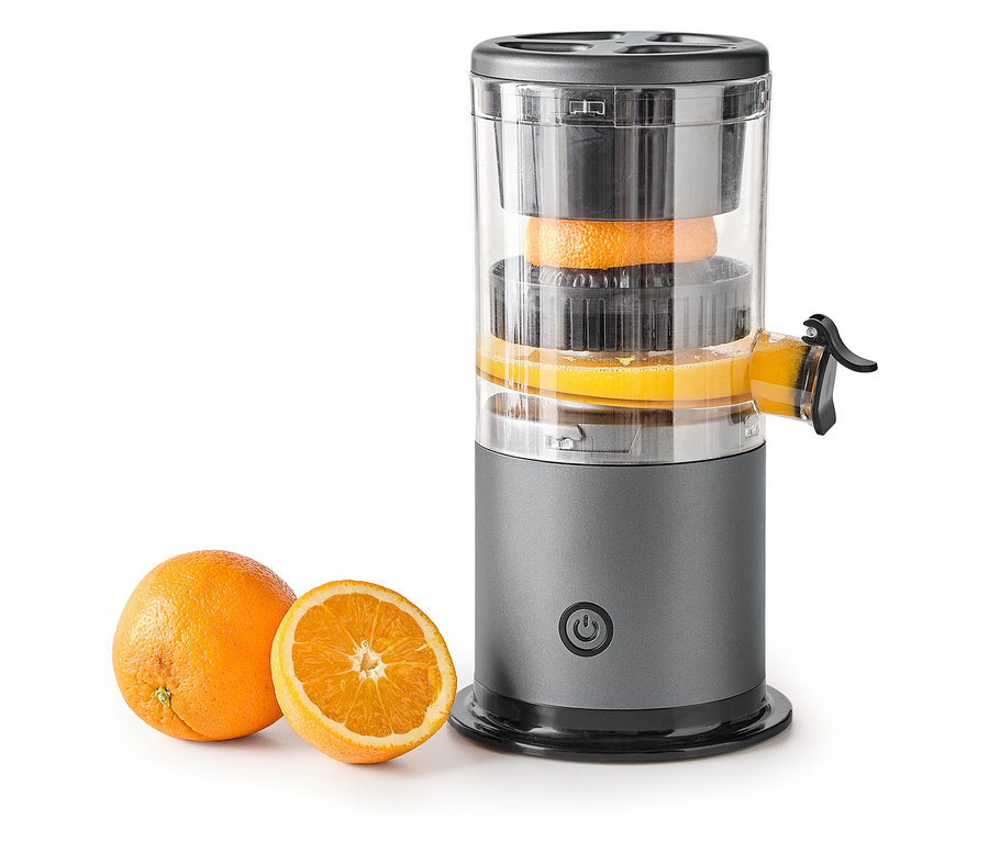 Des oranges sont pressées dans un presse-agrumes gris, à côté duquel se trouvent une orange entière et une demi-orange.