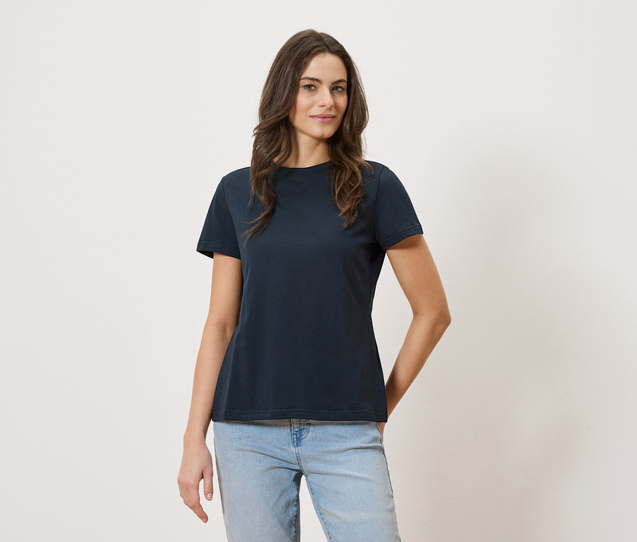 Une femme porte un t-shirt bleu marine et un jean sur un fond blanc.