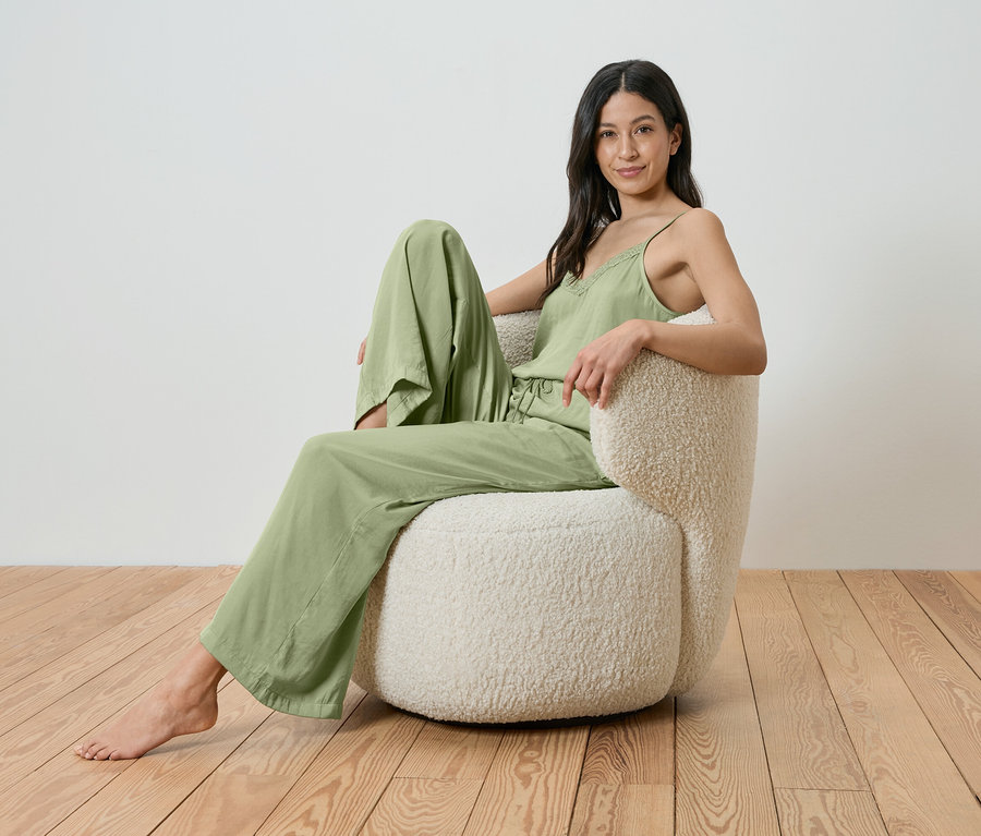 Une femme est assise pieds nus dans un fauteuil crème et porte un pyjama vert clair.