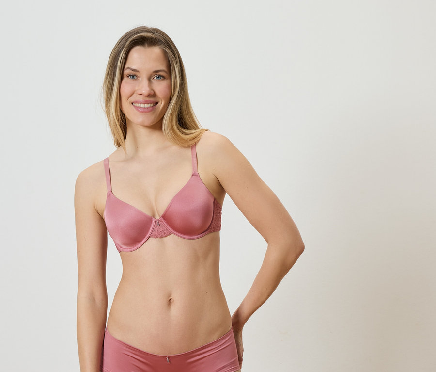 Une femme blonde portant un soutien-gorge et une culotte roses sur fond blanc.