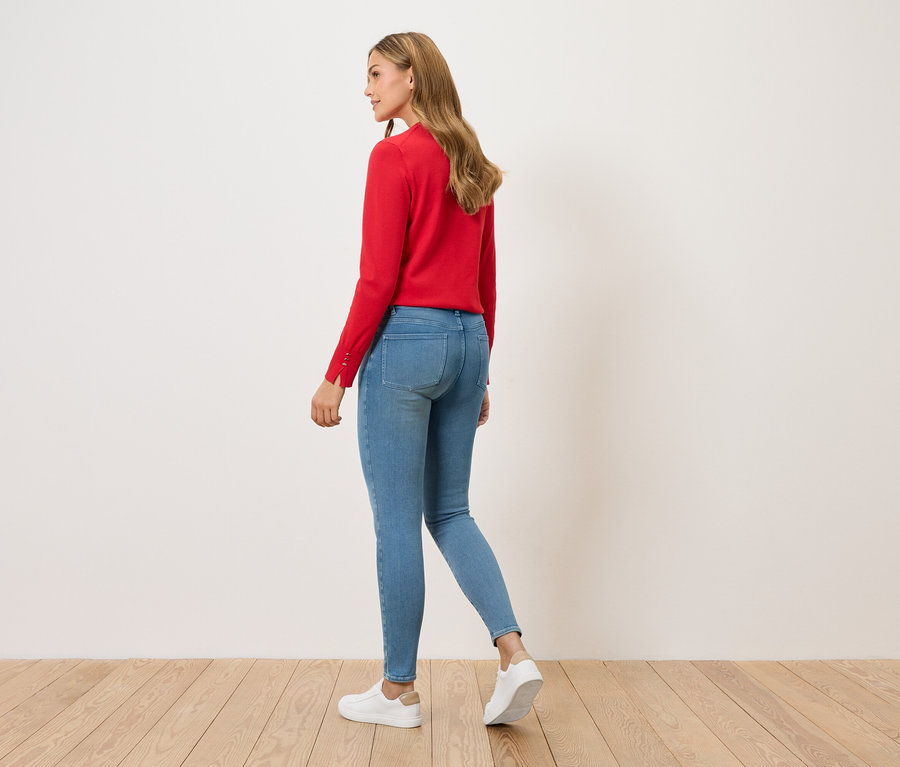 Femme marchant, vue de dos, portant un pull rouge, un jean bleu et des baskets blanches.