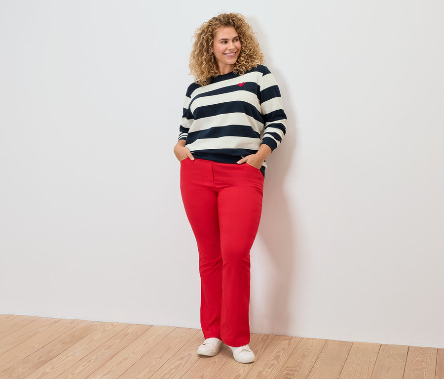 Une femme aux cheveux bouclés porte un haut rayé et un pantalon rouge.