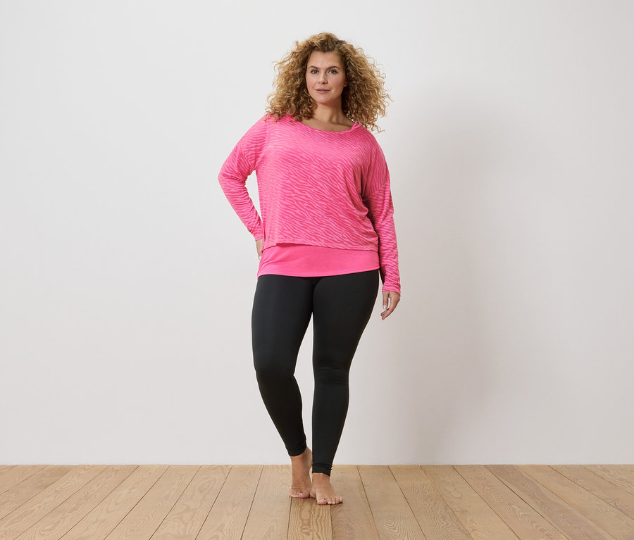 Femme aux cheveux bouclés portant un haut à manches longues zébré rose et un legging noir.