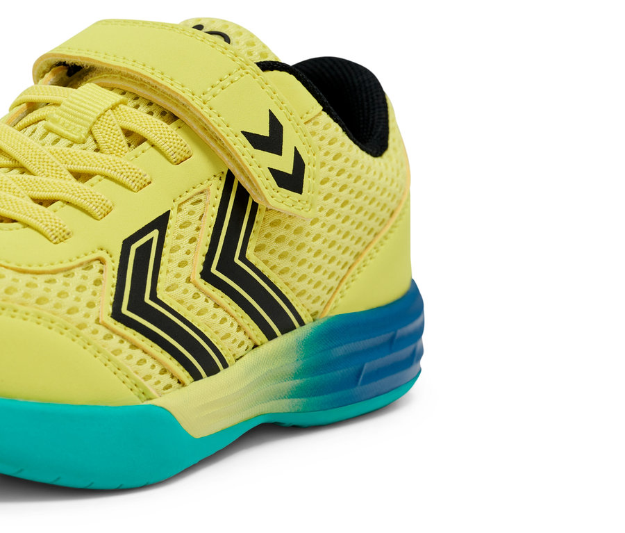 Gros plan d'une chaussure de sport jaune clair pour enfants avec fermeture velcro et chevrons Hummel noirs, la semelle est turquoise.