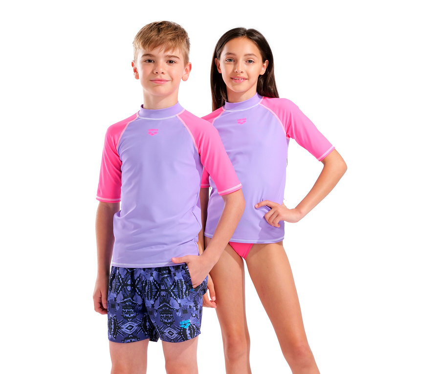 Un garçon en maillot de bain et une fille en bikini rose et t-shirts rashguard lilas se tiennent côte à côte.