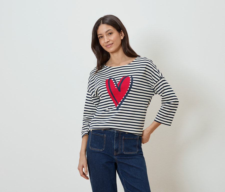 Femme portant un haut rayé à manches longues avec un cœur rouge et un jean.