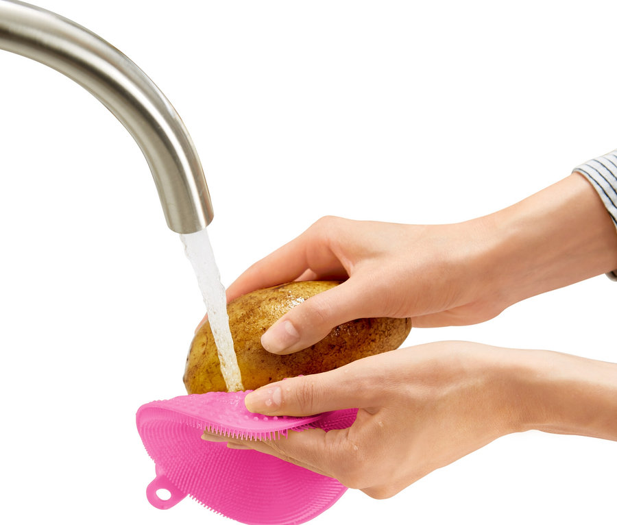 Une personne lave une pomme de terre avec une brosse rose sous un robinet.