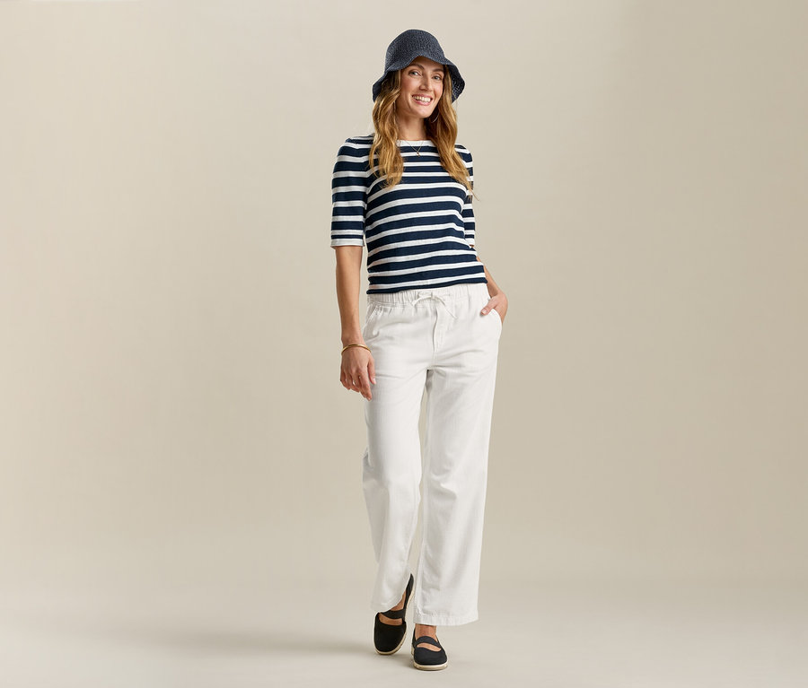 Une femme portant un chapeau, un T-shirt rayé et un Jeans grand confort pose avec une main dans sa poche.