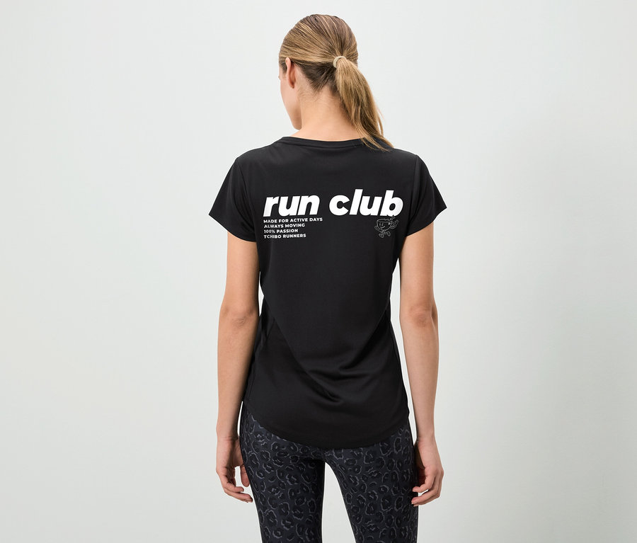 Vue arrière d'une femme portant un t-shirt noir avec l'inscription "run club" et un legging à motifs, les cheveux attachés en queue de cheval.