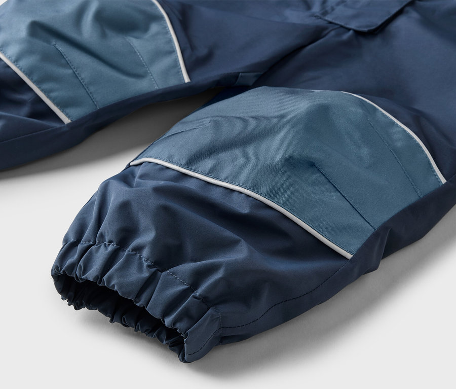 Gros plan d'un pantalon bleu marine avec des pièces aux genoux bleu clair et des accents blancs, posé sur une surface plane.