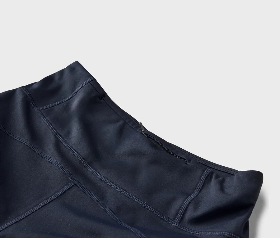 Gros plan sur un tissu de sport bleu foncé avec des coutures visibles et une petite poche zippée près de la ceinture.