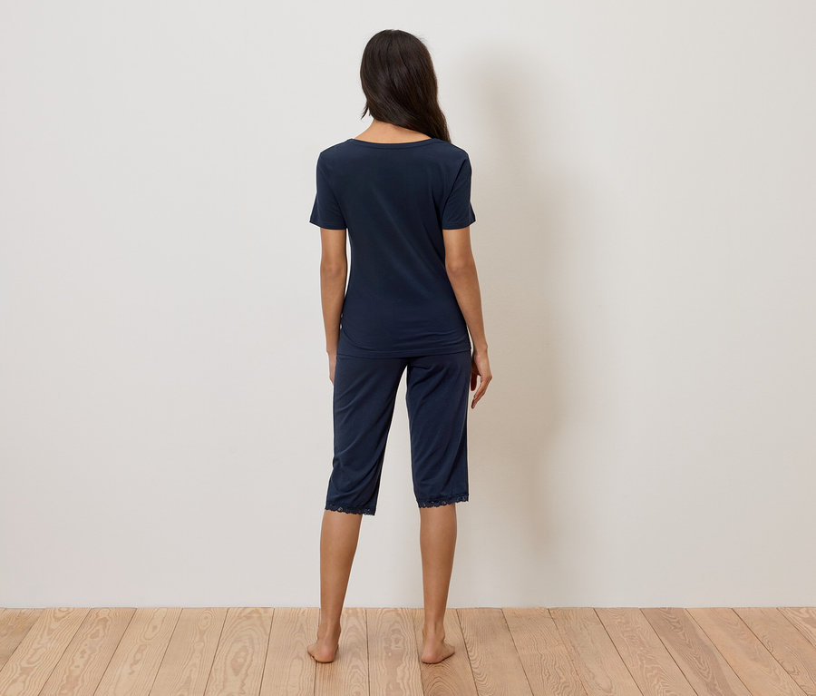 Une femme, vue de dos, porte un pyjama bleu marine avec des détails en dentelle.