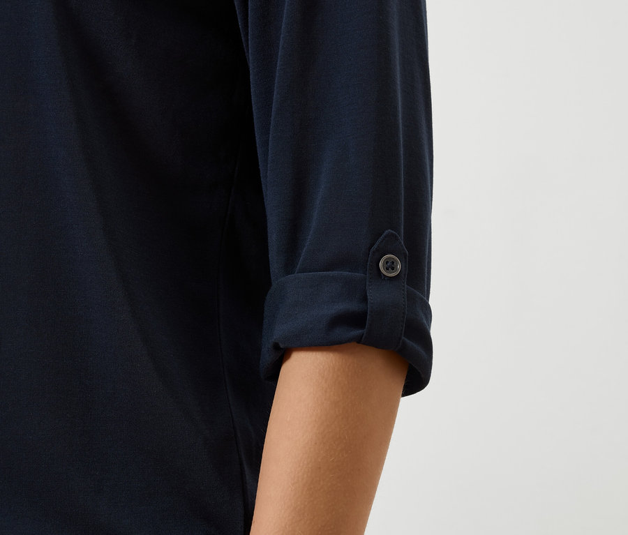 Gros plan sur la manche d'une chemise bleu marine retroussée et boutonnée.