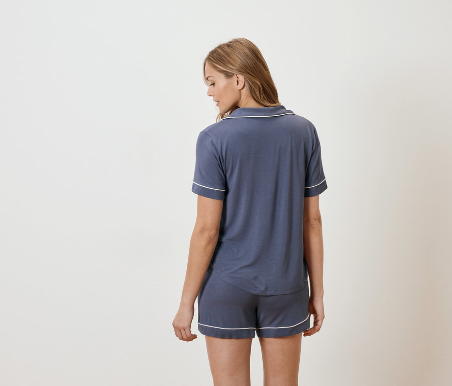 Femme vue de dos en pyjama bleu marine à manches courtes avec passepoil blanc.