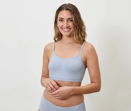 Femme souriante aux cheveux ondulés portant un soutien-gorge bleu clair à fines bretelles et des sous-vêtements assortis.