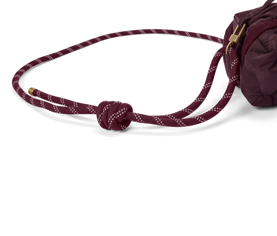 Gros plan d'un sac matelassé bordeaux avec un cordon de serrage bordeaux noué.