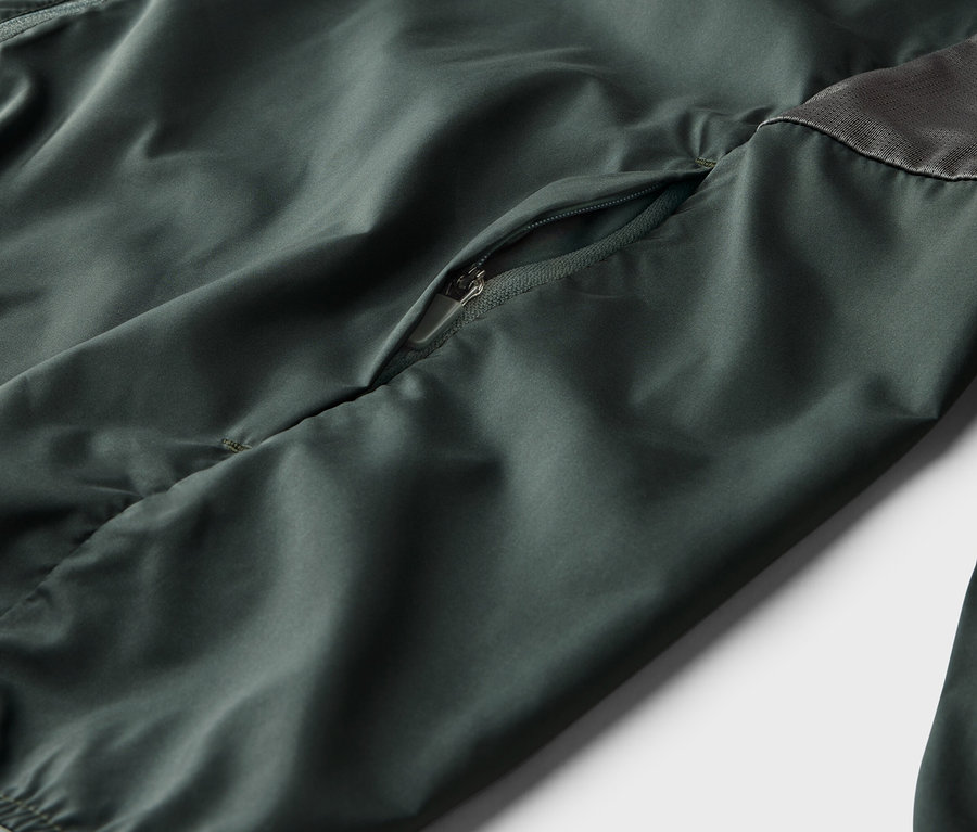 Gros plan d'une veste vert olive avec une poche zippée et un empiècement en maille grise.