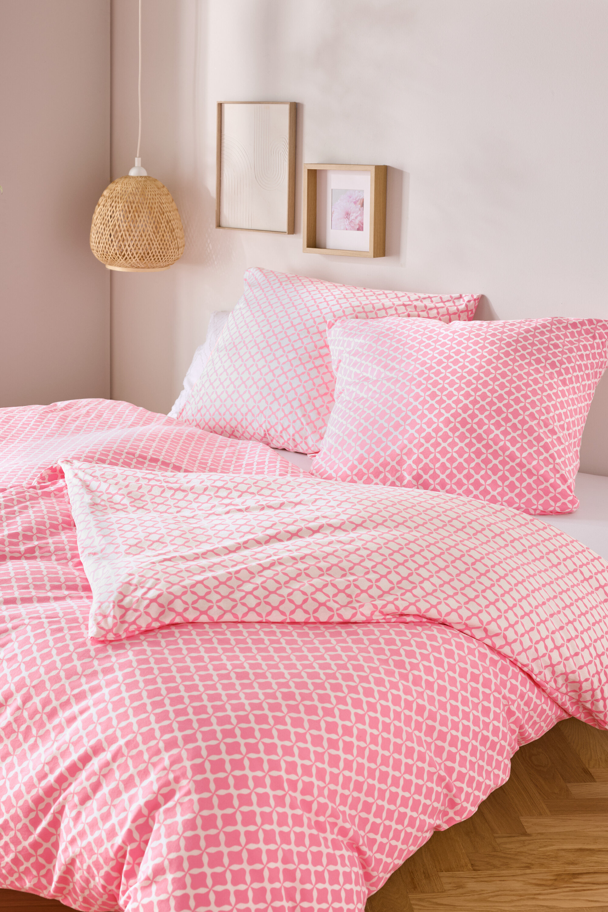 Gros plan d'un lit avec du linge de lit en jersey rose et blanc, taille standard et king size, avec deux oreillers et une couette.